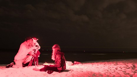 Three people take light measurements of the sky at night.