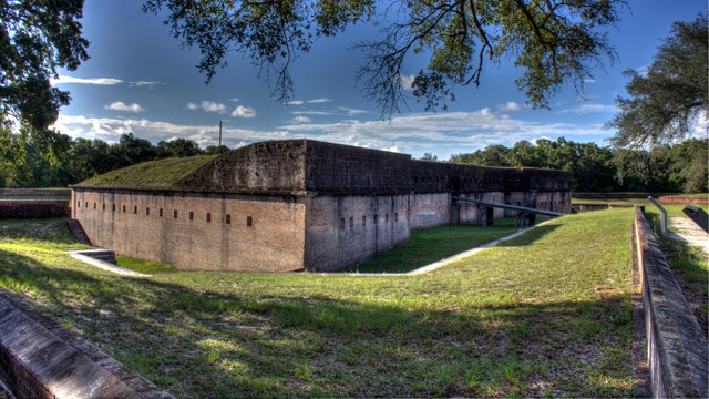 A masonry fort stands in a terraced field of grass.