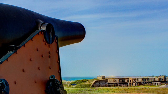 A large cannon sits on top of a historic fort with the coast in the background.