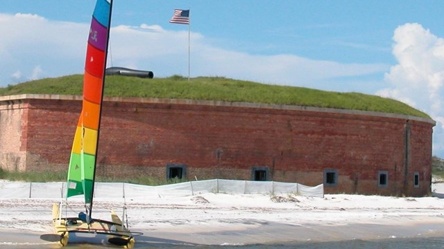 A colorful sailboat is beached in front of a large brick fort.
