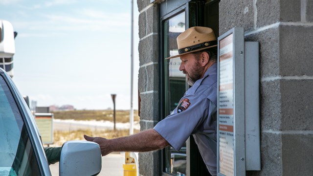 A ranger hands a pass back to a visitor in a vehicle.