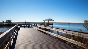 A large boardwalk and pavilion stands over still blue water.