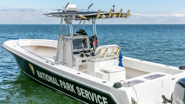 A National Park Service boat rests on top of blue green water.