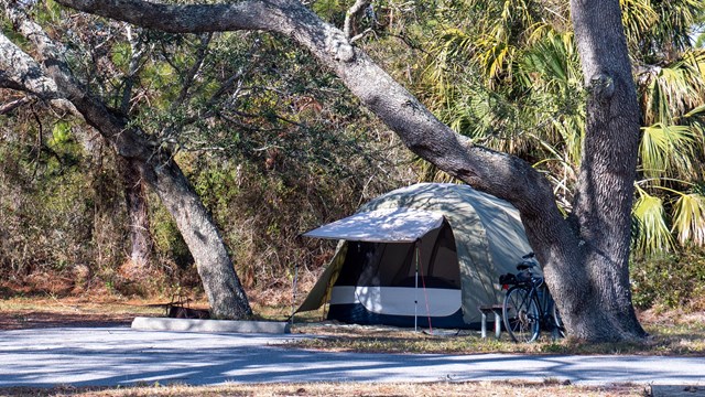 A sign that says, "Happy Campers Welcome" in the foreground and a camper in the background.