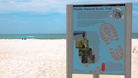 A sign for the Florida National Scenic Trail stands with the beach in the background.