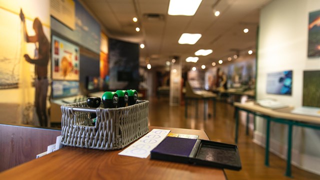 A basket of stamps and ink sits on top of a desk with exhibits in the background.