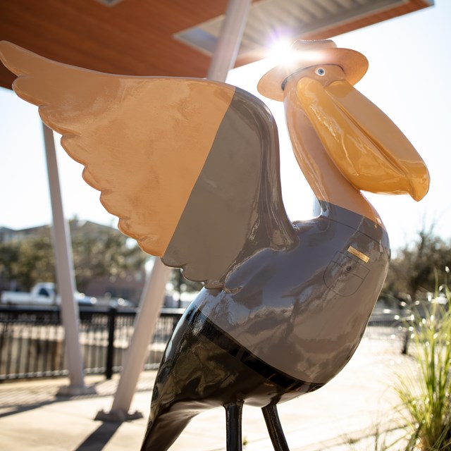 A pelican statue dressed as a ranger stands with the sun shining through its wings.