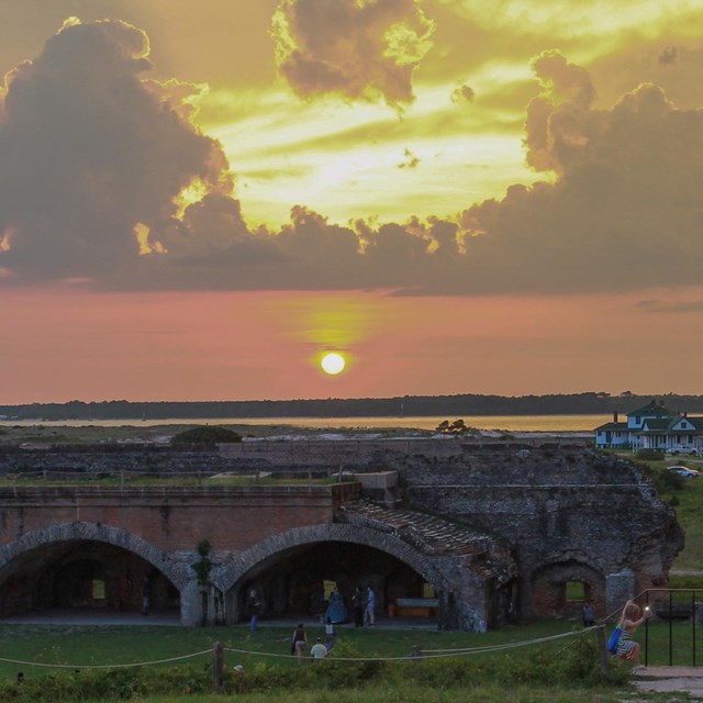 The sun sets behind a large masonry fort.