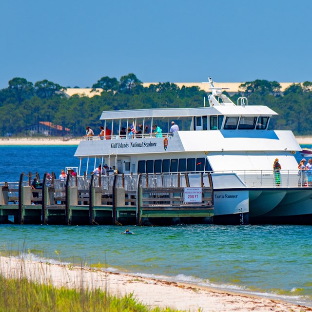 A ferry boat loads passengers over bright blue water.