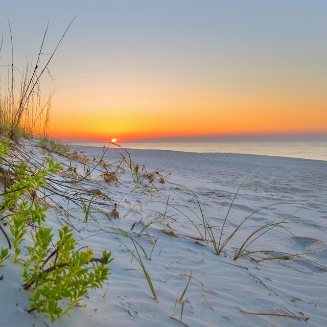 The sunrises over a white sand beach.