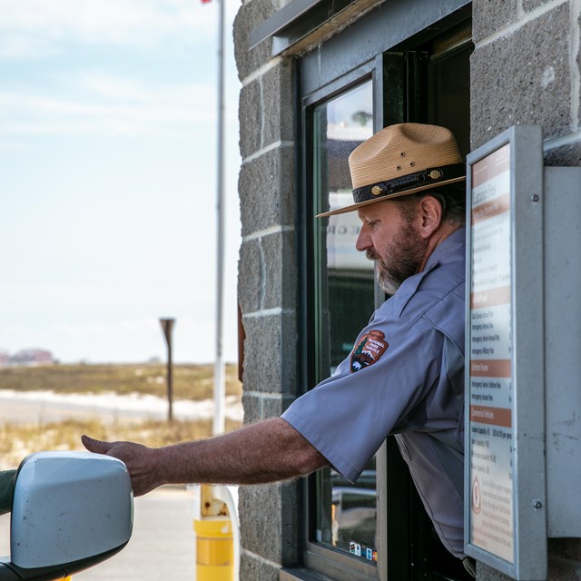 A ranger hands a pass back to a visitor in a vehicle.