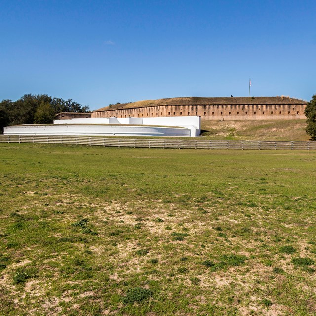 A large masonry fort sits on a hill above a white painted fort.