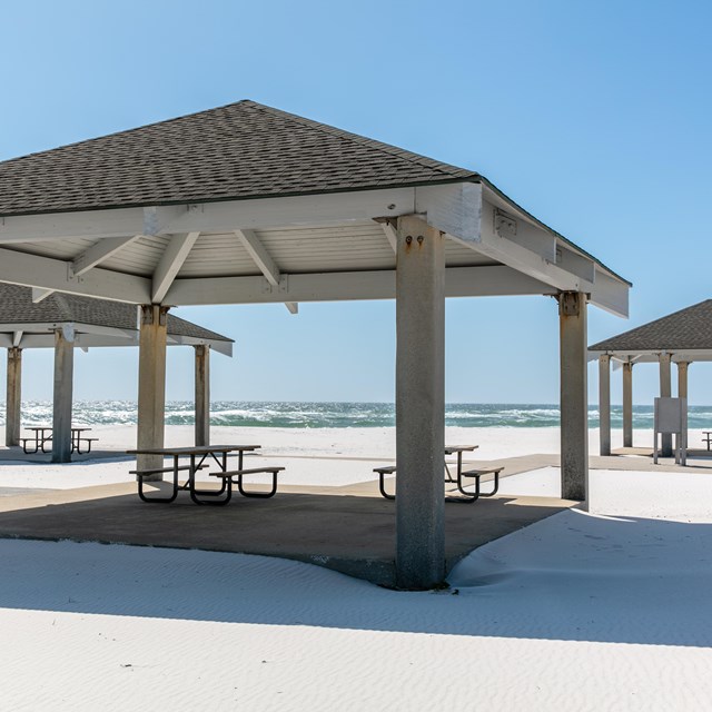 A group of pavilions stands on the edge of a sandy beach.