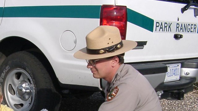 A park ranger kneels next to a patrol vehicle