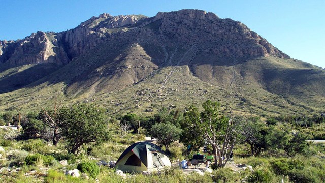 A tent stands in a pad below a large desert mountian.