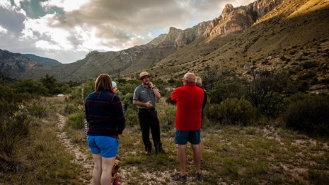 A park ranger speaks to a group of visitors as the sun sets over the mountains