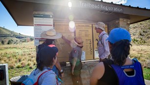 A ranger points to a trailhead map for a group pf hikers