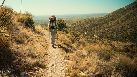 A hiker on a trail leading out of the desert into the mountains