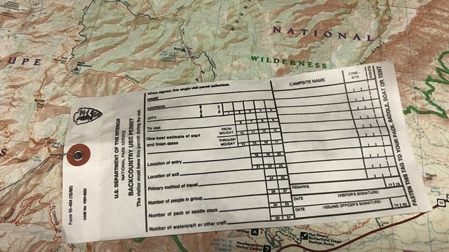 A paper permit form is on top of a topographic map of the park. 