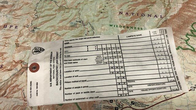 A papper permit form is on top of a topographic map of the park.