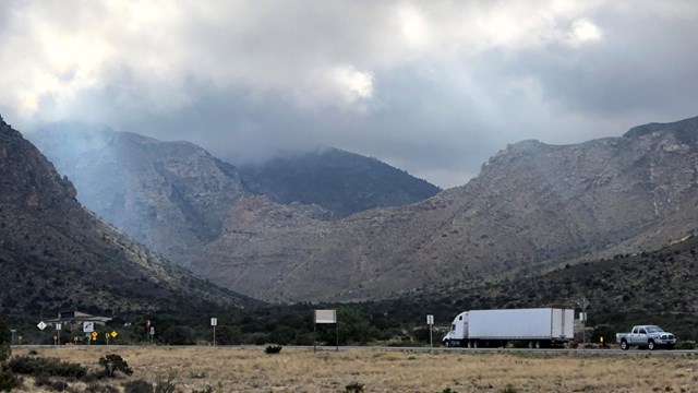 Highway traffic passes in front of a desert mountain canyon