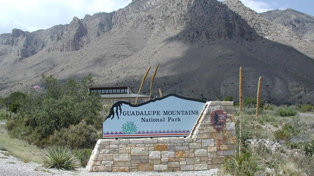 A park entrance sign in front of the visitor center and the mountains