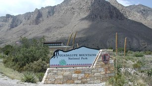 A park entrance sign in front of the visitor center and the mountains