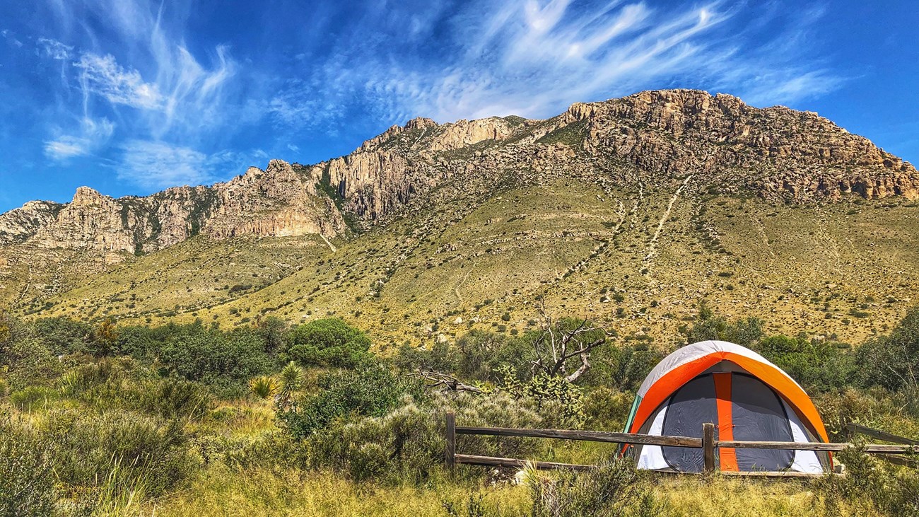 A bright tent in a tent campsite with mountains behind it.