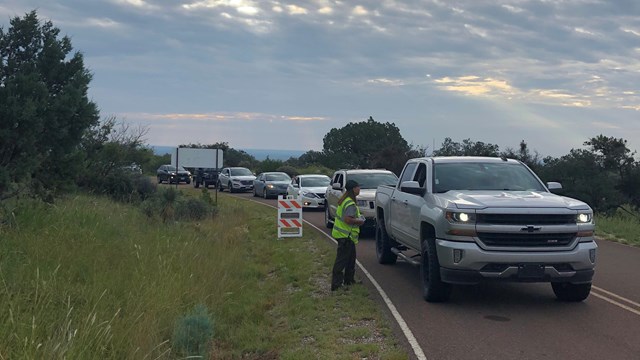 A uniformed ranger in a safety vest talks to the occupants of a pickup at the lead of a line of cars