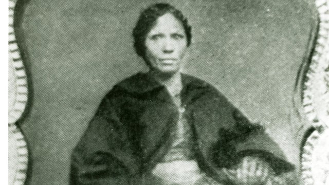 A portrait of an African American woman sitting and wearing a black shawl. 