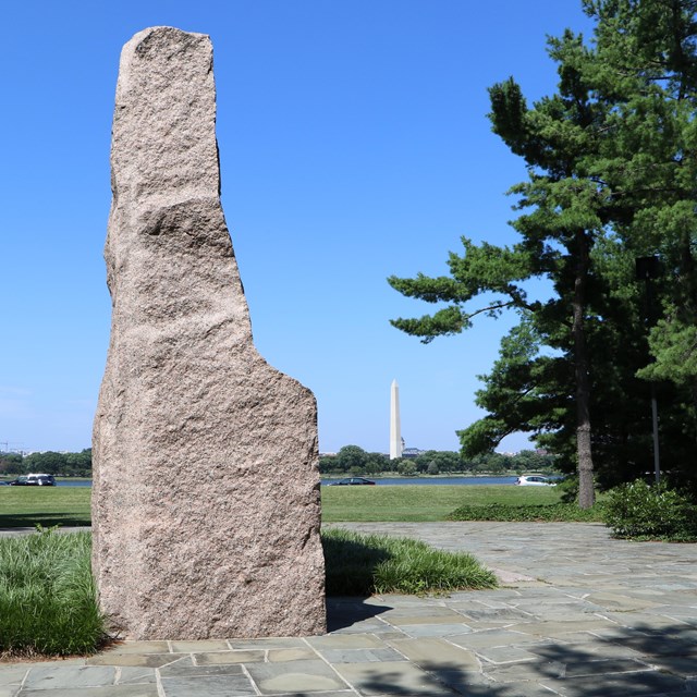 A stone plinth with the Washington Monument across a river in the background.