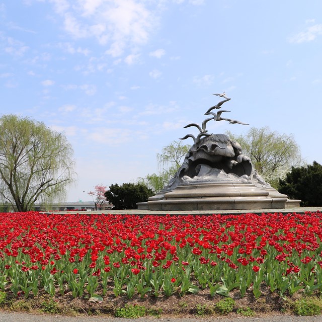 A statue of waves and gulls with red flowers in the foreground.