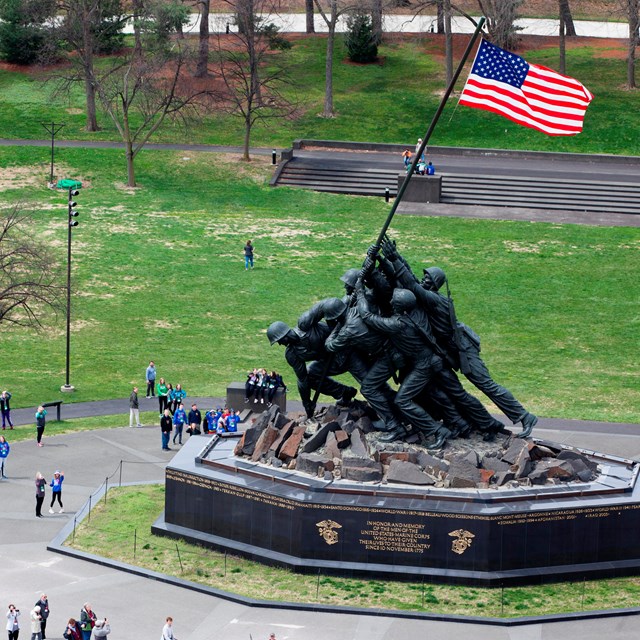 An aerial view of a large bronze memorial of marines raising a US flag surrounded by a paved plaza.