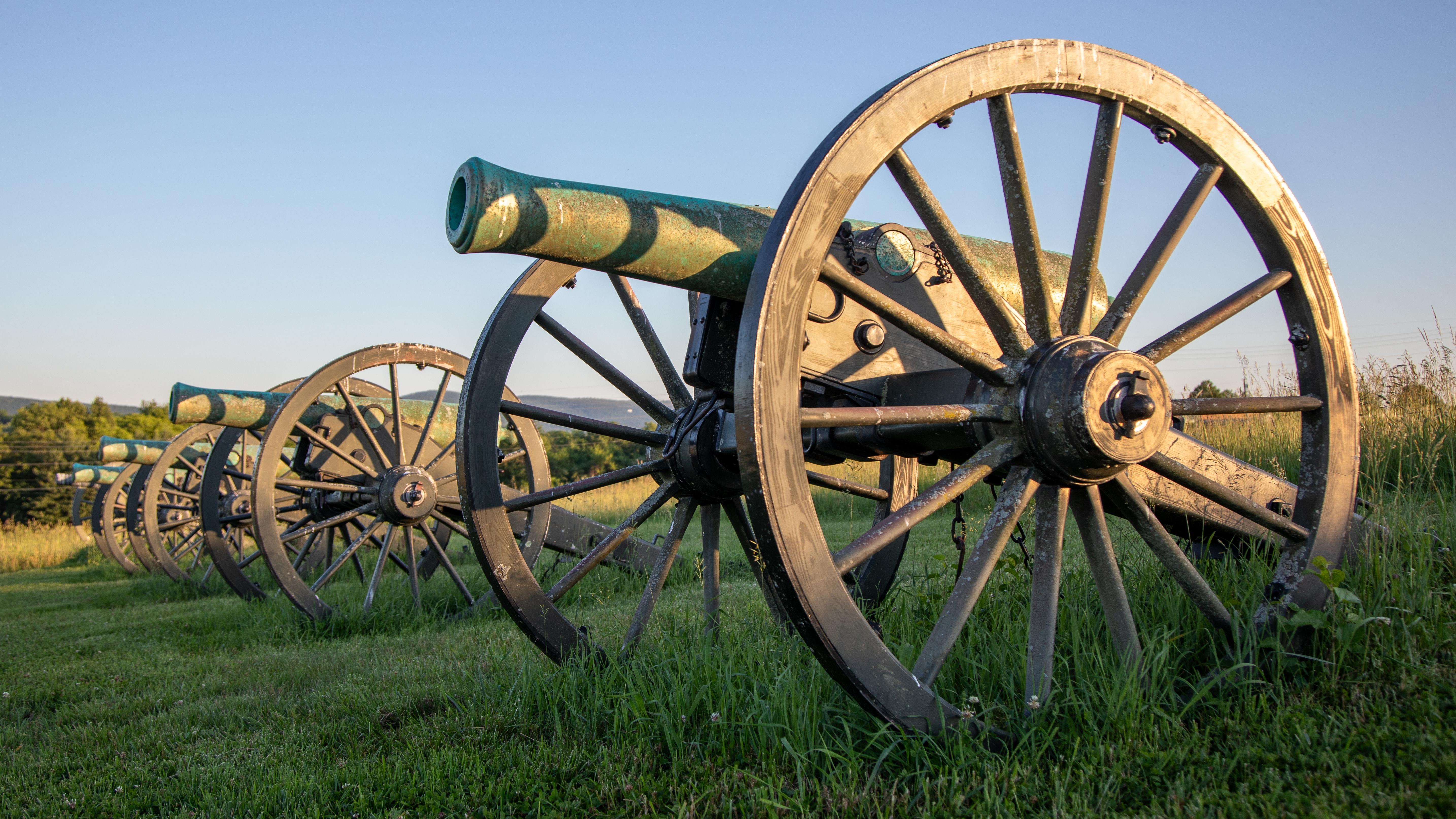 A line of cannon in a field at sunset.