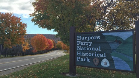 A large sign beside a winding rural road reads Harpers Ferry National Historical Park