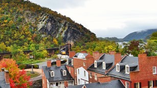 Lower Town in the fall. Brick buildings, trees with changing leaves, train emerging from rocky hill.