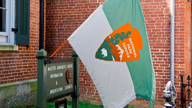 photo of a National Park Service flag attached to a information sign; background is a brick building