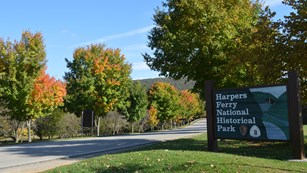 road lined with trees starting to turn fall colors; entrance sign to the right states the park name