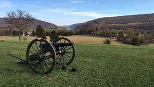 an artillery piece on the fall landscape; in the distance is a gap in the mountains