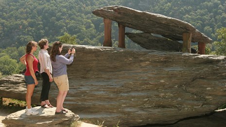 three women stand looking at Jefferson Rock; one is taking a photo of it