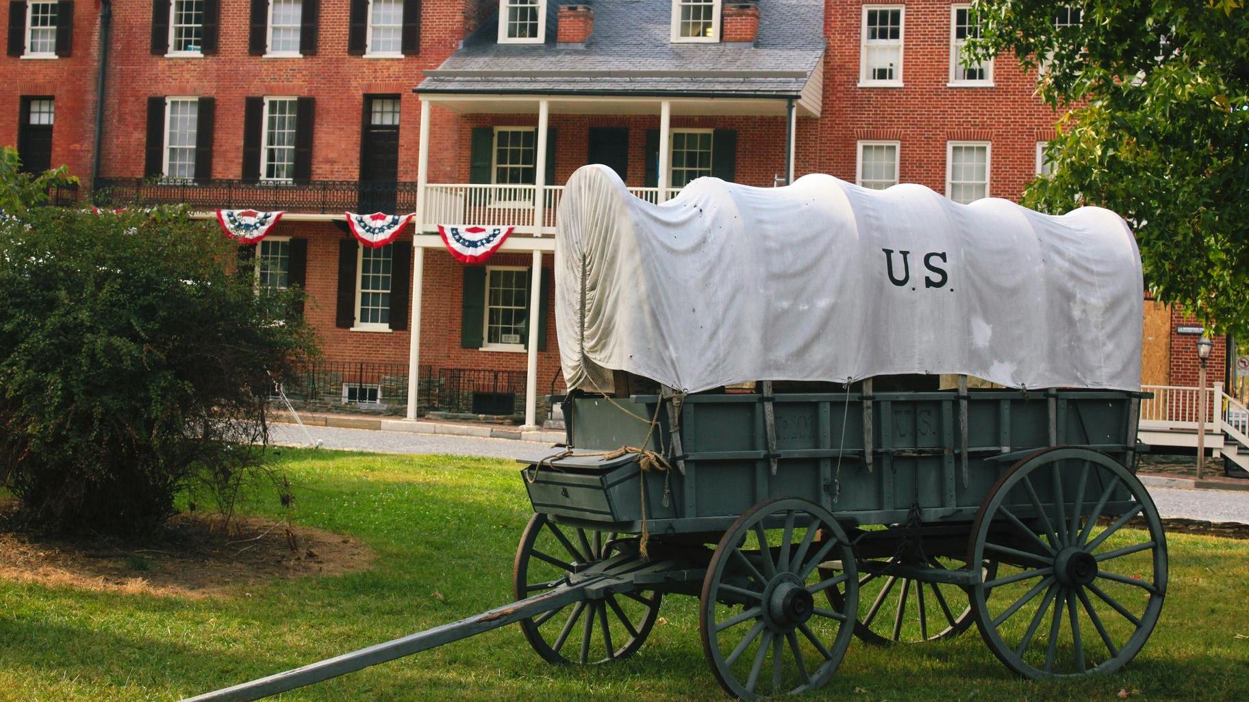 A historic wagon on a lawn in front of brick buildings. 