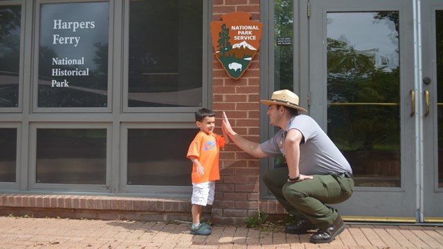 park ranger and young boy high five in front of the park visitor center