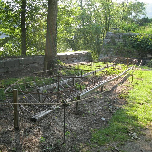 Metal boat frame surrounded by rope in a walled grassy area