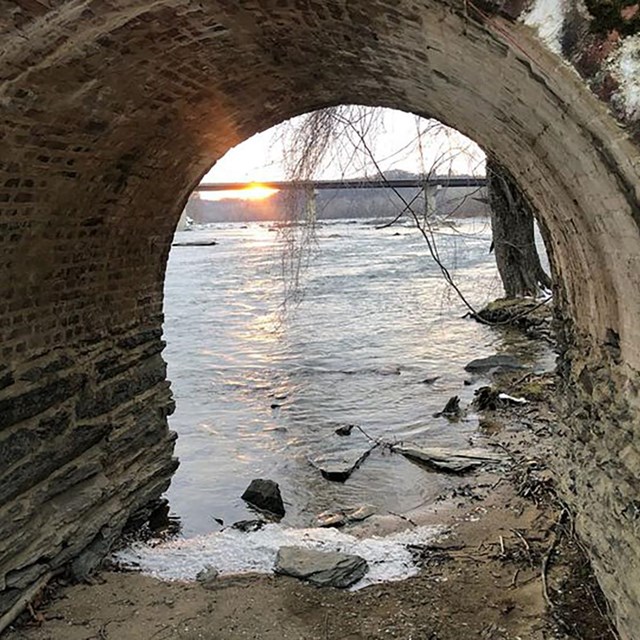 View through an arched brick and stone structure to a river at sunset
