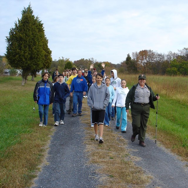 Group of school-age youth walk on path with female park ranger