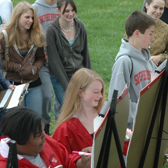 Group of school-age youth gathered around large writing pads