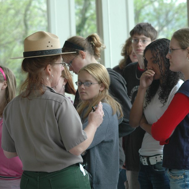 Group of school-age youth gathered around a female park ranger