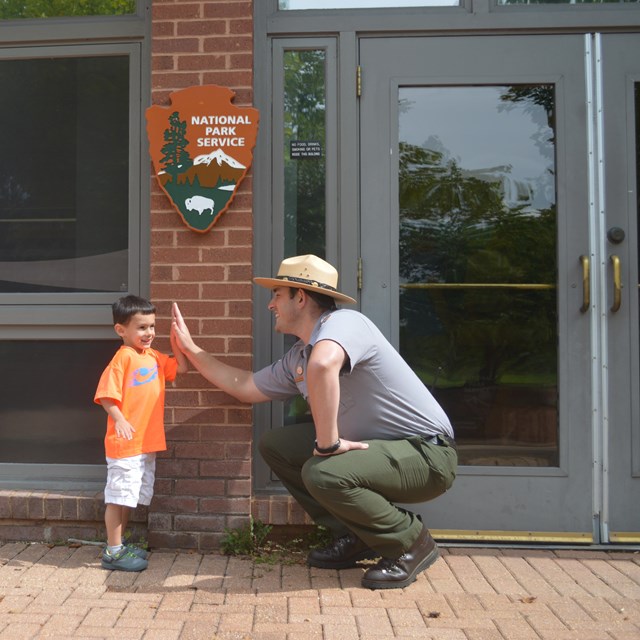 park ranger and young boy high five in front of the park visitor center