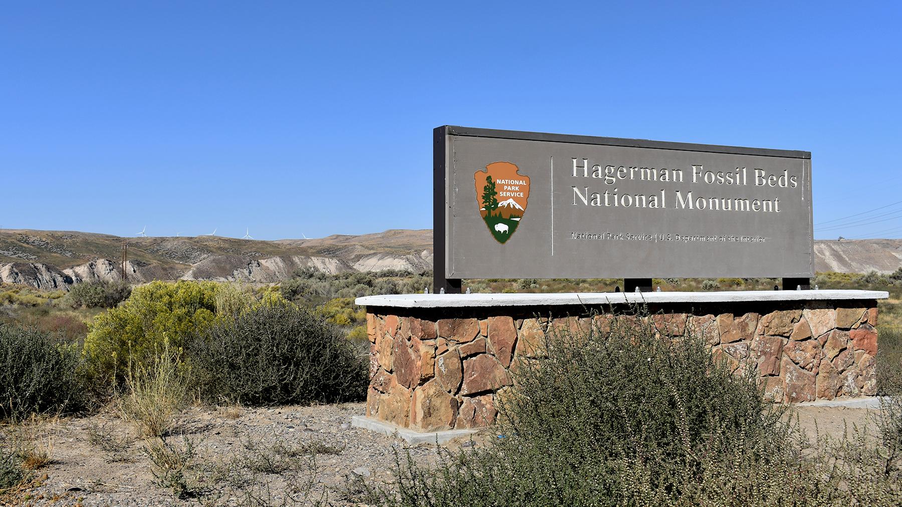 Photo of the Hagerman Fossil Beds entrance sign, with the fossil beds in the distant background.