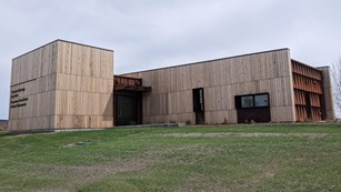 A boxy, wood-paneled visitor center sits atop a grassy slope.